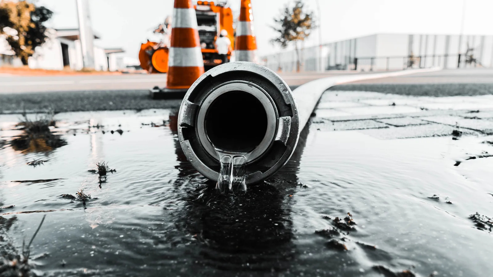 A discharge hose running water out across a road behind traffic cones