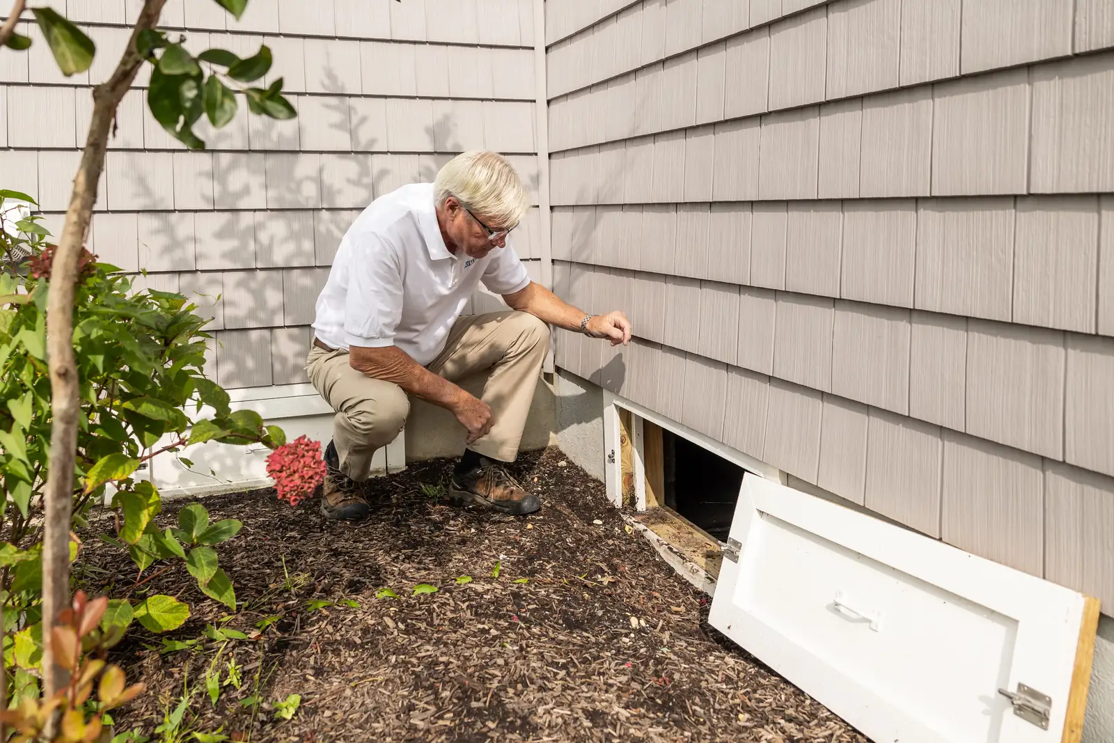 An inspector checking an access hatch at the base of a house