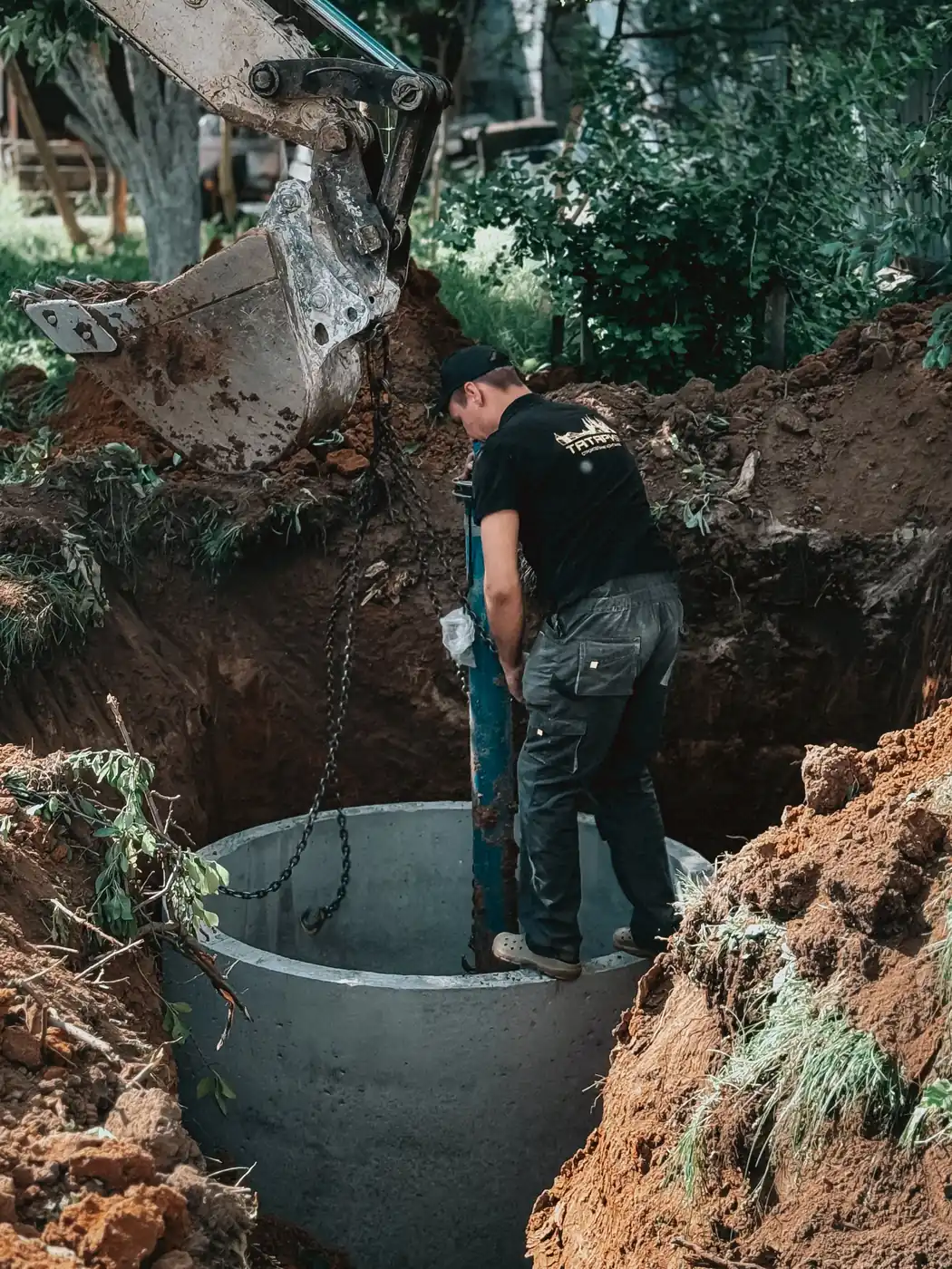 An excavator lowering a concrete chamber into an open excavation